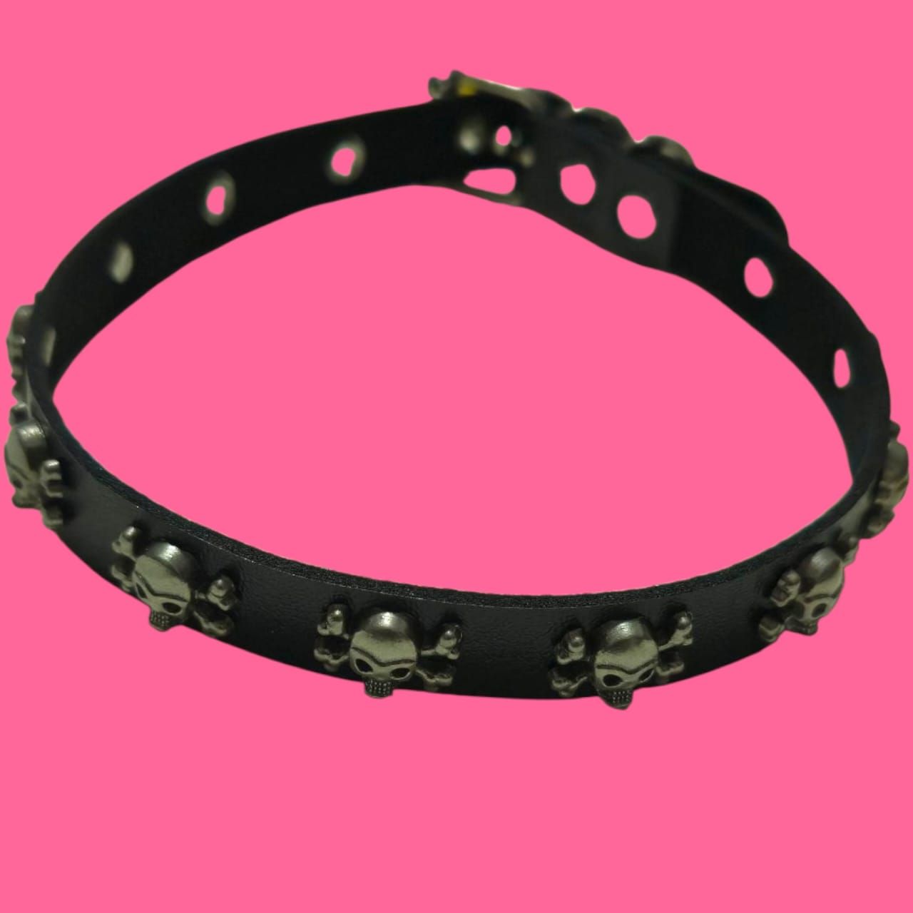 Gargantilla de cuero negro con calaveras plateadas, fondo rosa.