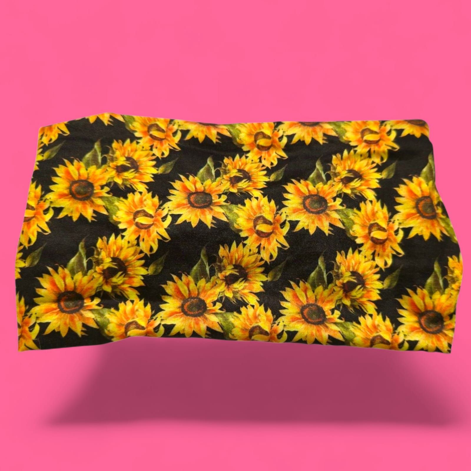 Tela negra con girasoles amarillos sobre fondo rosa brillante.