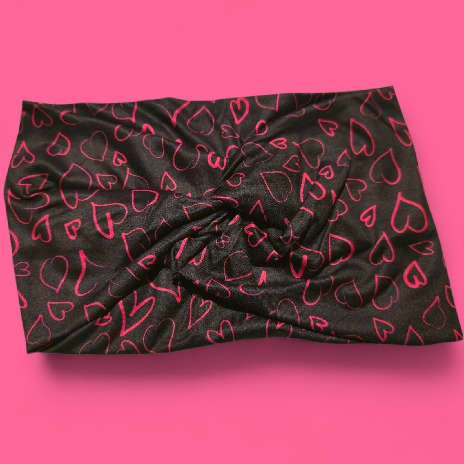 Diadema negra con garabatos de corazones rosas sobre un fondo rosa.