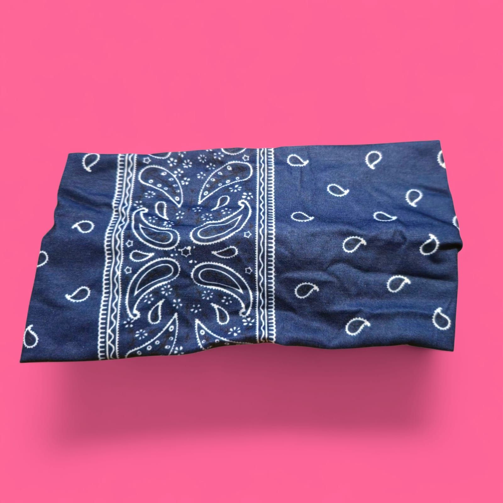 Pañuelo azul con estampado paisley blanco, doblado sobre fondo rosa.
