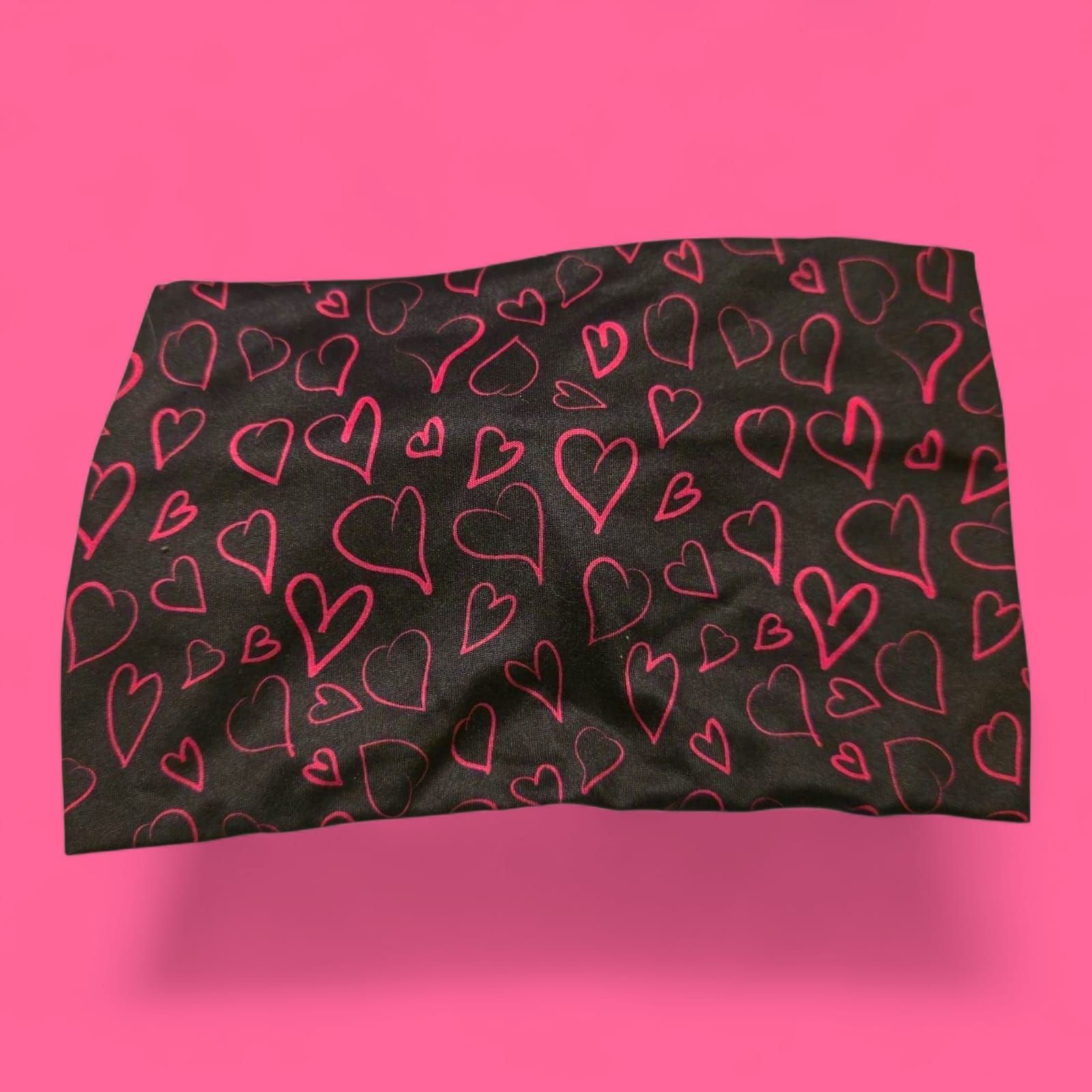 Diadema negra con garabatos de corazones rosas sobre un fondo rosa.