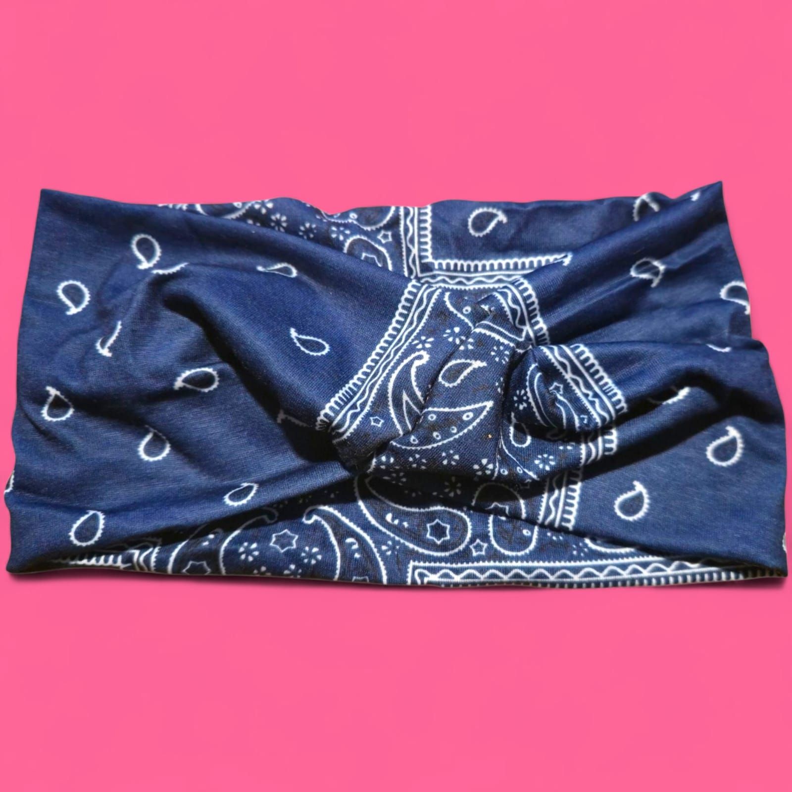 Pañuelo azul con estampado paisley blanco, doblado sobre fondo rosa.