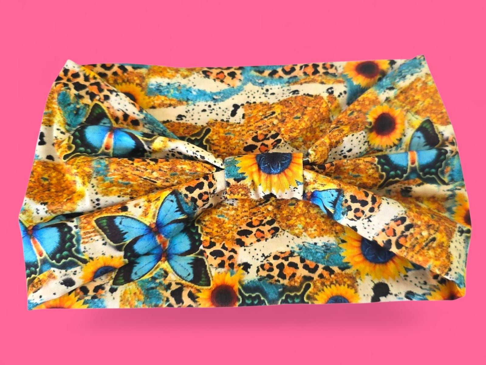Tela colorida con mariposas azules, girasoles y estampado de leopardo sobre fondo rosa.