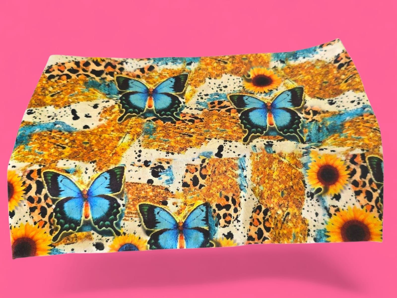 Tela colorida con mariposas azules, girasoles y estampado de leopardo sobre fondo rosa.