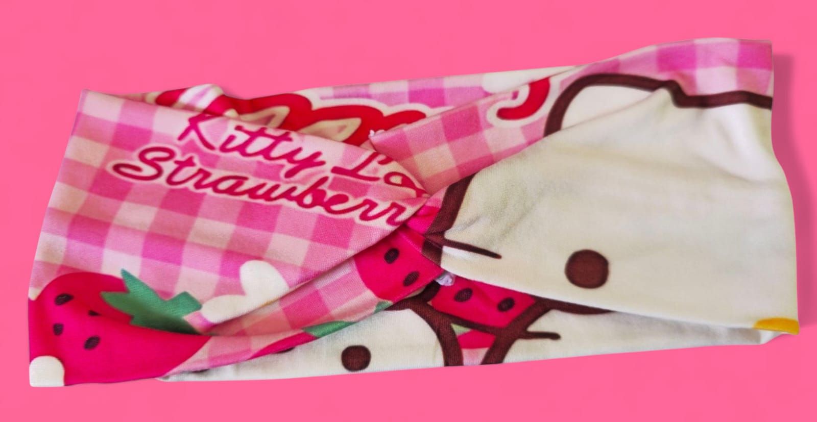 Toalla de Hello Kitty con fresas sobre fondo de cuadros vichy rosas.