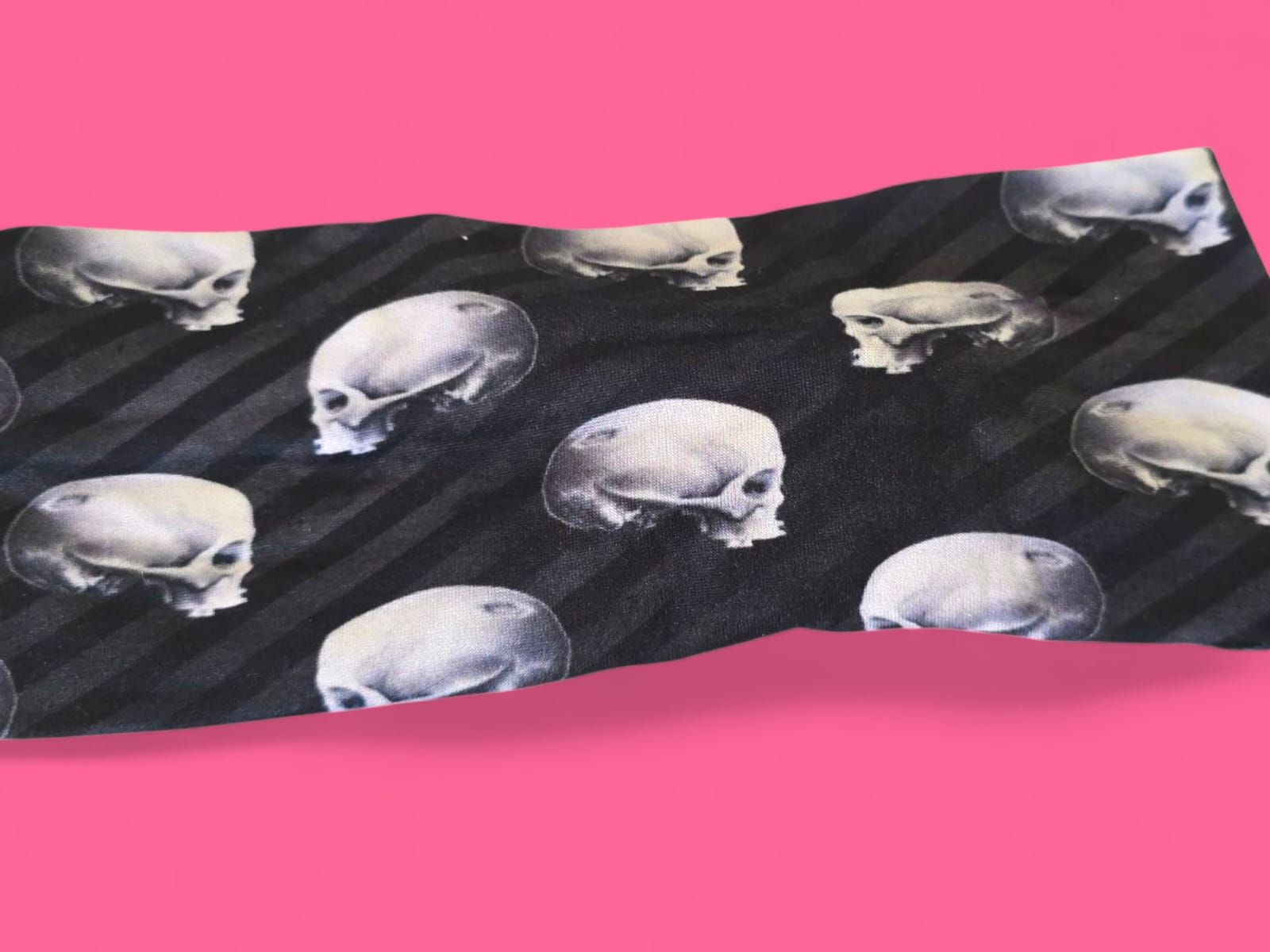Corbata negra con estampado de calavera y rayas grises sobre fondo rosa.