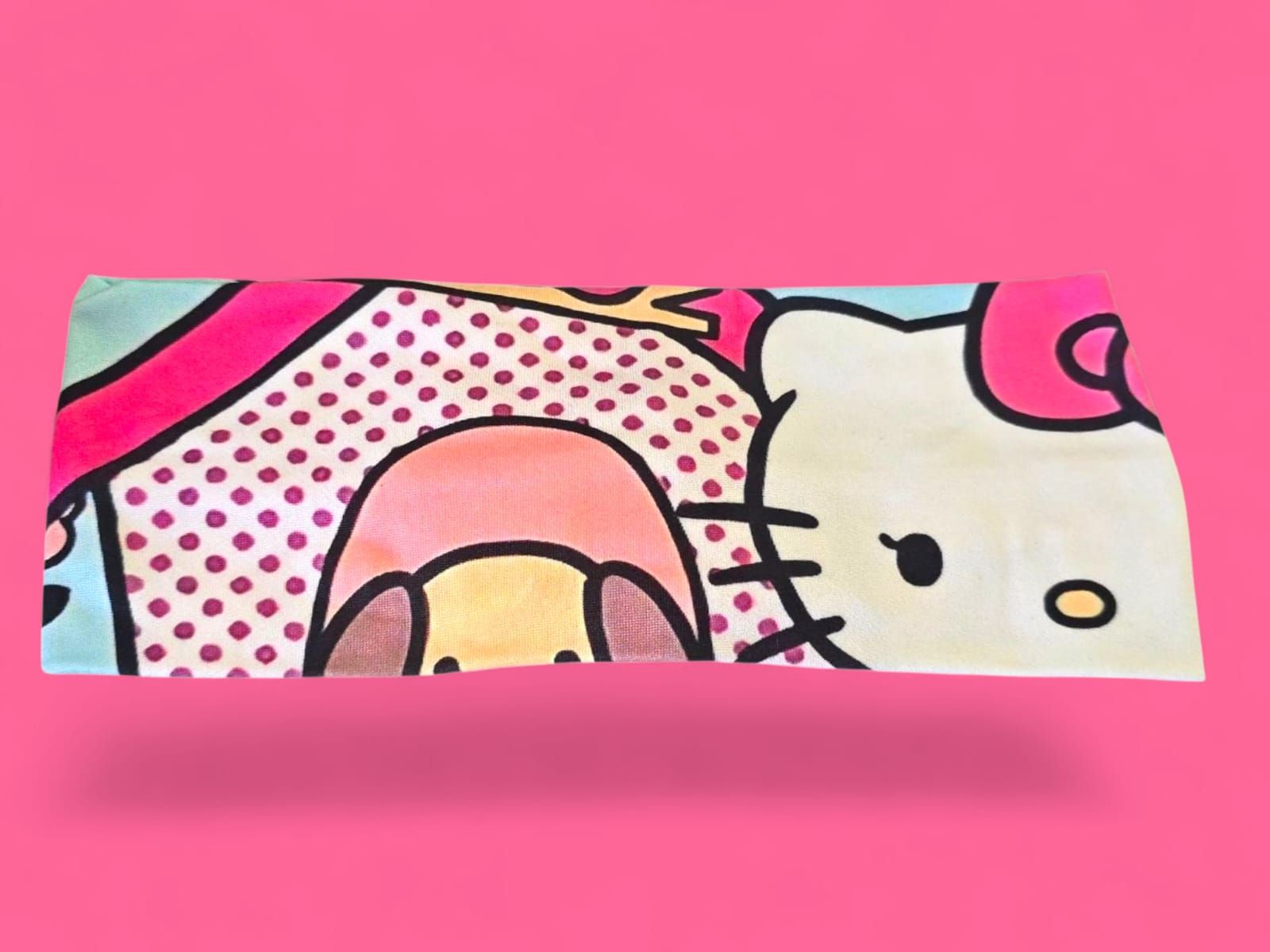 Toalla de Hello Kitty, color rosa y azul claro, con dibujo de perro y lunares, sobre fondo rosa.