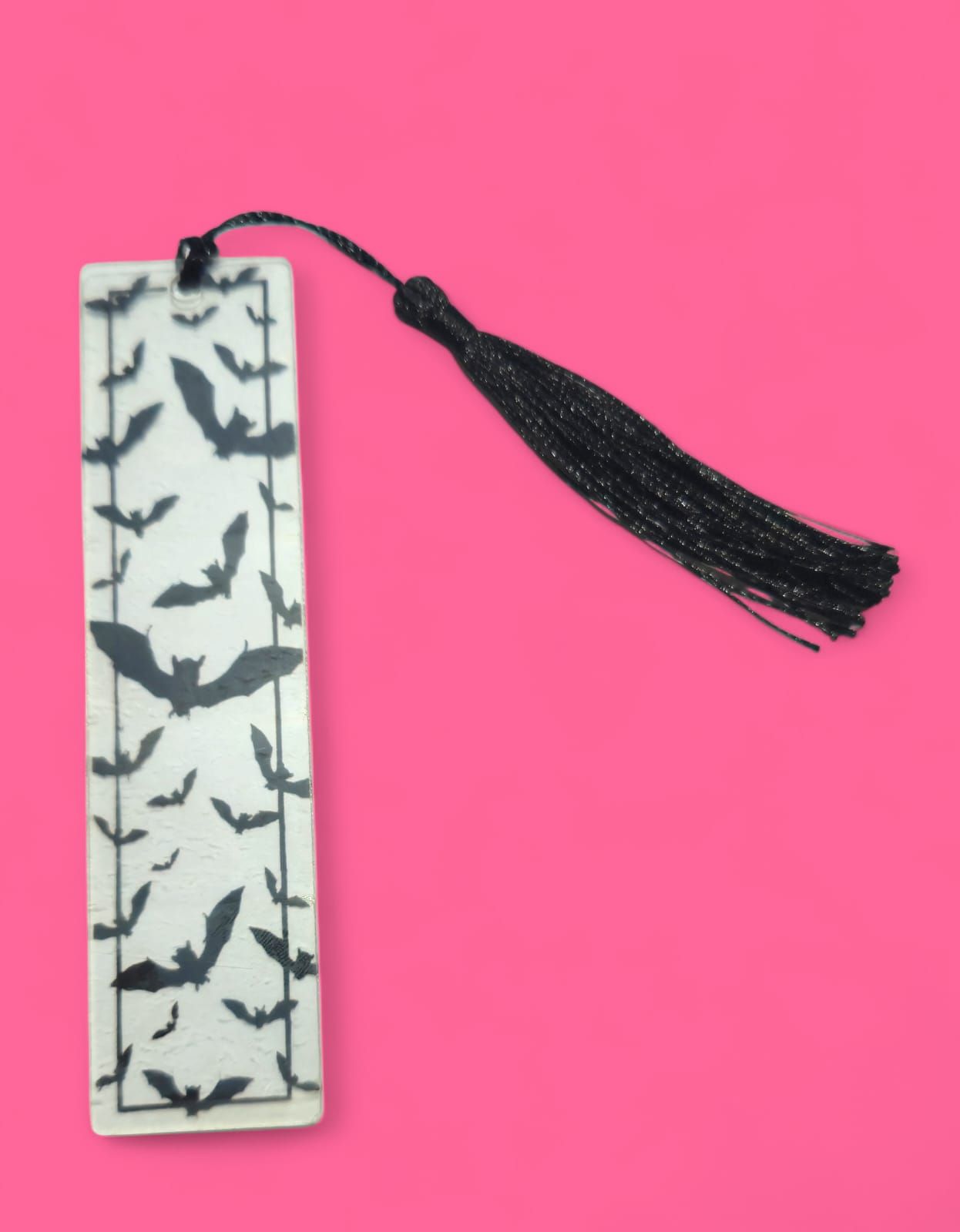 Marcador con murciélagos negros sobre fondo blanco, borla negra, sobre fondo rosa.
