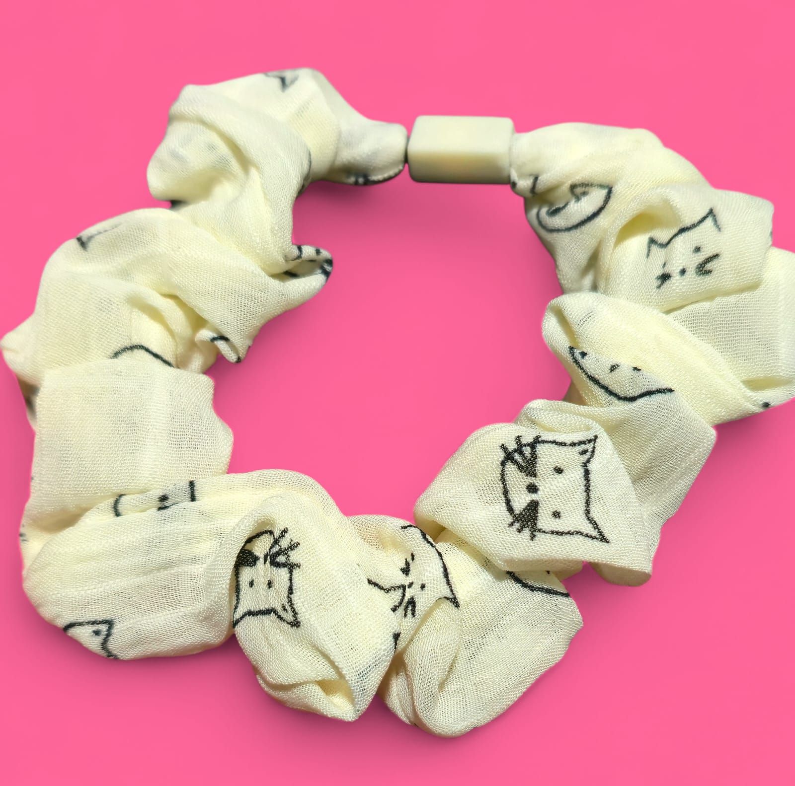 Coletero con estampado de gato amarillo y cierre en color neutro sobre fondo rosa.