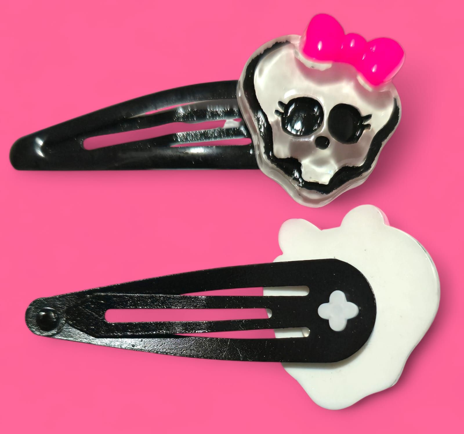 Dos pinzas negras para el pelo con diseños de Monster High. Una tiene una calavera y un lazo rosa, y la otra un fantasma.