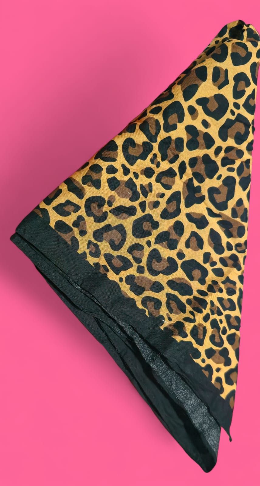 Bandana con estampado de leopardo, ribete negro, doblada y fondo rosa.