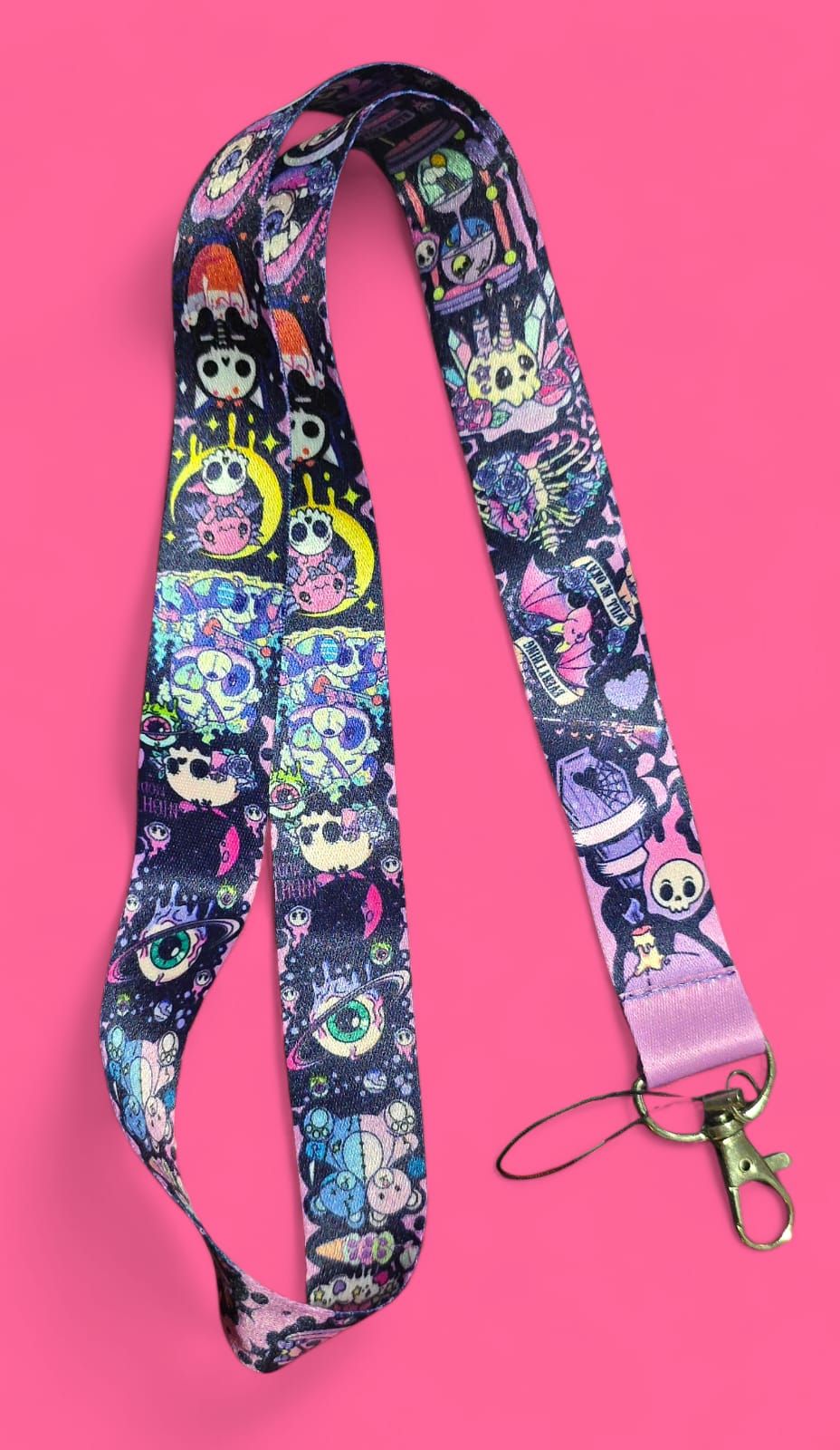 Cordón con diseño de fantasía repetida sobre fondo morado oscuro. Cierre de mosquetón morado y lazo rosa.