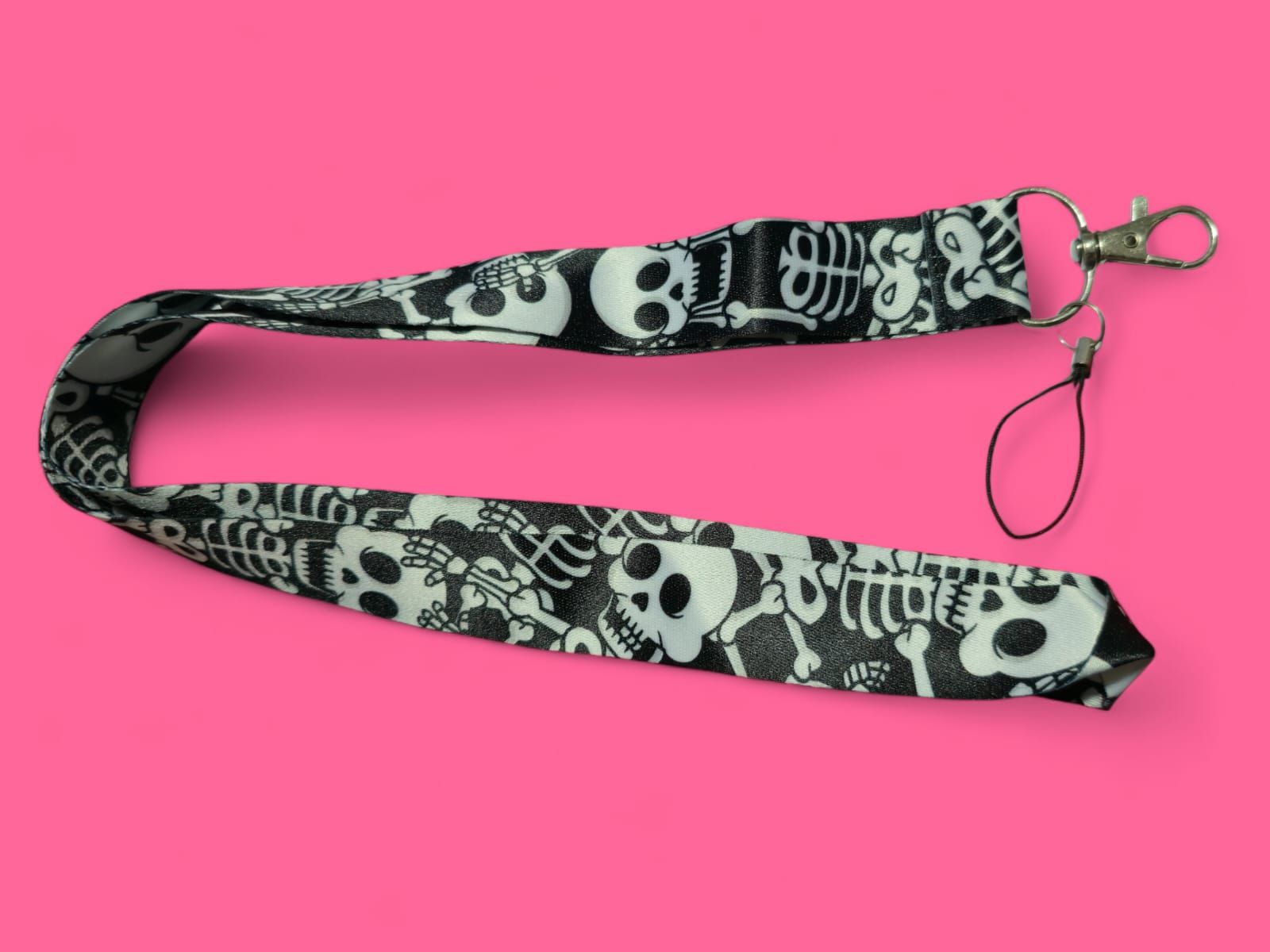 Cordón con estampado de calavera y esqueleto en blanco y negro con cierre plateado sobre fondo rosa.