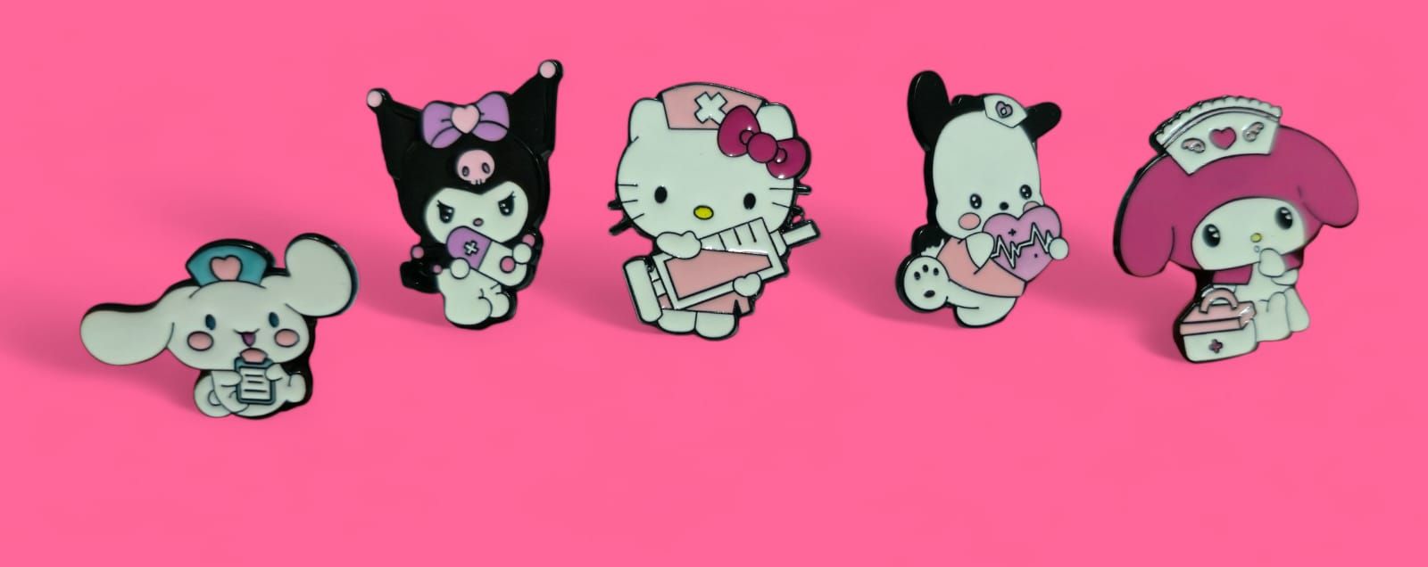 Cinco pins de personajes de Sanrio sobre un fondo rosa: Cinnamoroll, Kuromi, Hello Kitty, Pompompurin y My Melody.