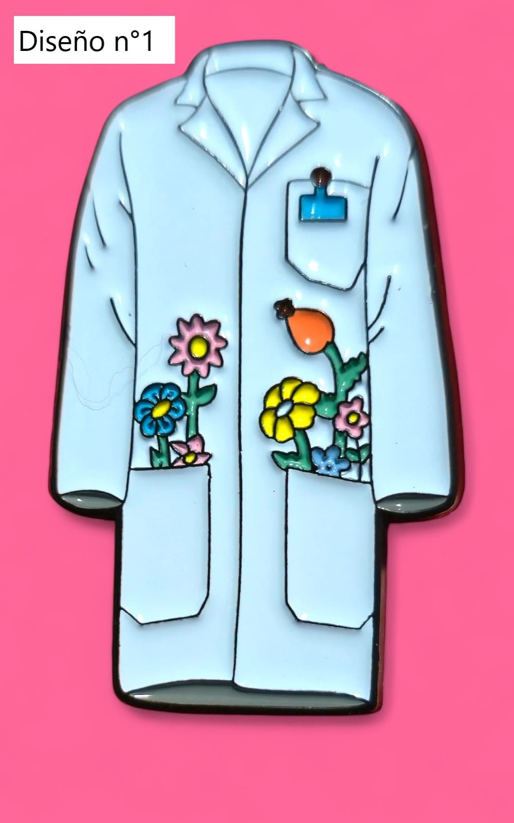 Cinco pins esmaltados sobre fondo rosa: bata de laboratorio, tubo de ensayo, átomo, gato y microscopio.