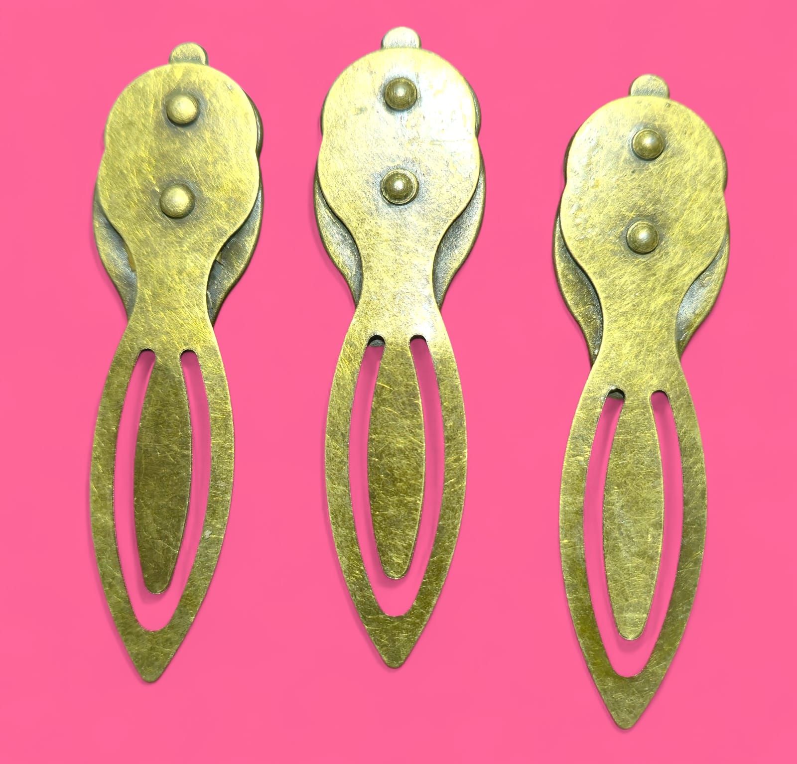 Tres marcadores de bronce con tapas ornamentadas: cuervo, mariposa monarca y mariposas rojas.