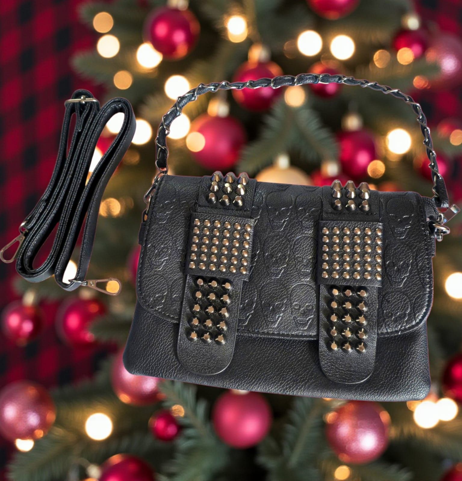 Bolso de mano negro con tachuelas y correa de cadena, sobre un fondo de árbol de Navidad borroso.