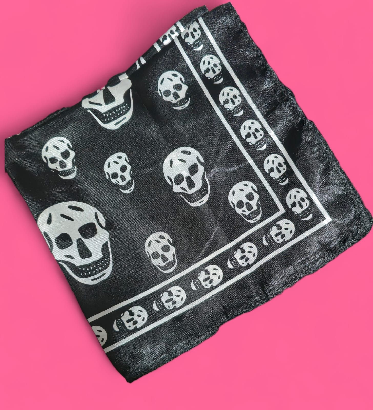Pañuelo negro con estampado de calavera blanca sobre fondo rosa.
