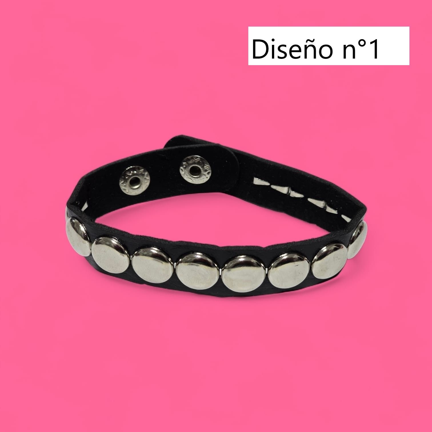 Pulsera con tachuelas negras sobre fondo rosa.