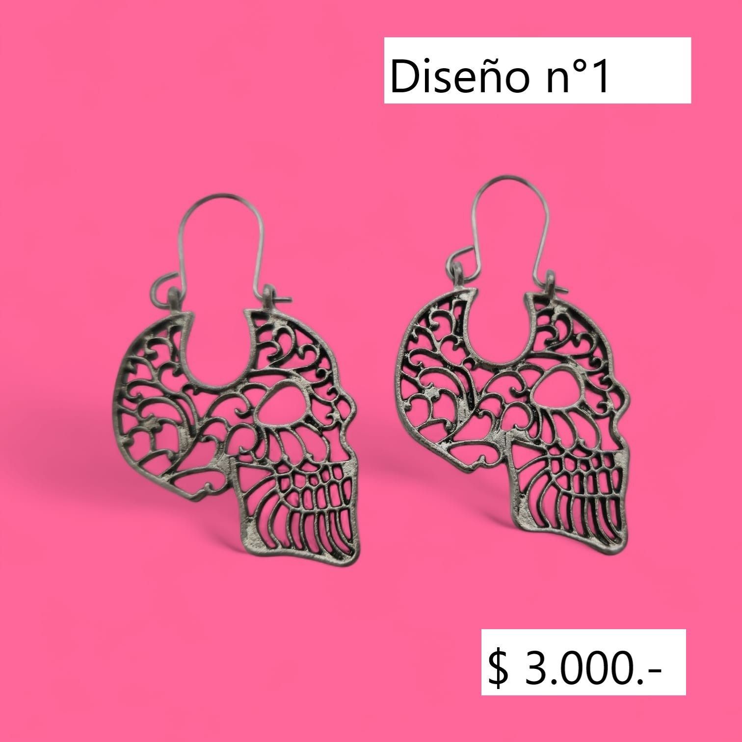 Par de pendientes de plata en forma de calavera sobre fondo rosa con etiqueta con precio.