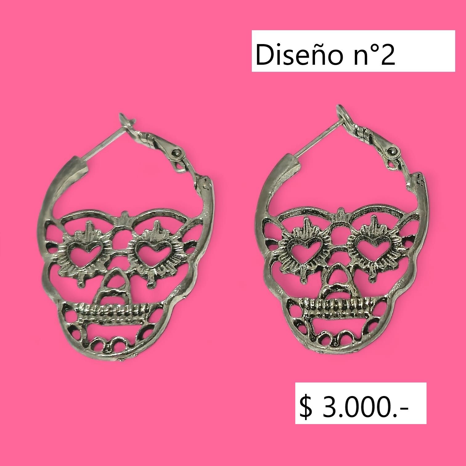 Par de pendientes de plata en forma de calavera sobre fondo rosa con etiqueta con precio.