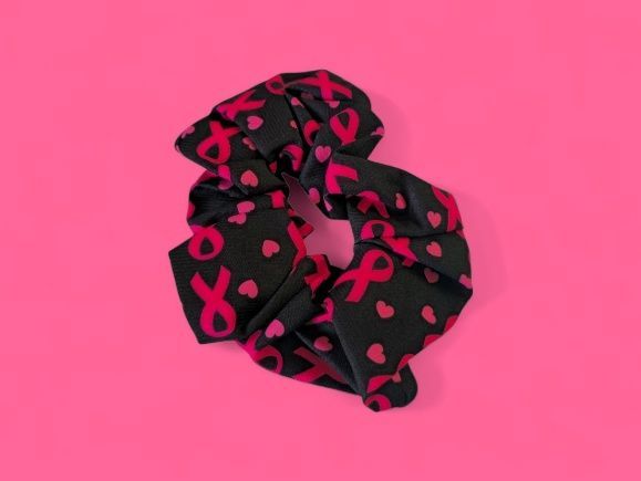 Coletero negro con cintas rosas de concienciación sobre el cáncer y corazones sobre un fondo rosa.