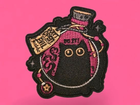 Gato negro en una burbuja, con un sombrero de copa rosa y negro. La etiqueta dice: "No abras el mal".