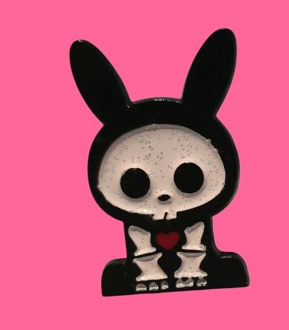 Conejito blanco y negro con un traje de calavera, sosteniendo un corazón rojo sobre un fondo rosa.