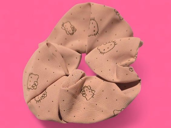 Coletero beige con estampado de Hello Kitty sobre fondo rosa.