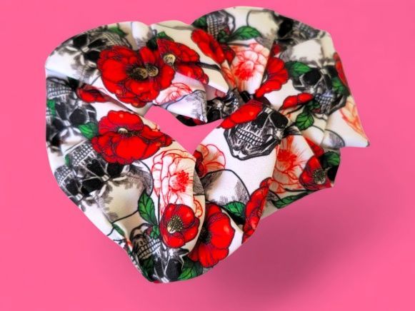 Coletero con estampado de calavera y flores rojas sobre fondo blanco, sobre un fondo rosa.