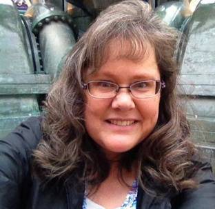 A woman wearing glasses and a black jacket is smiling for the camera.