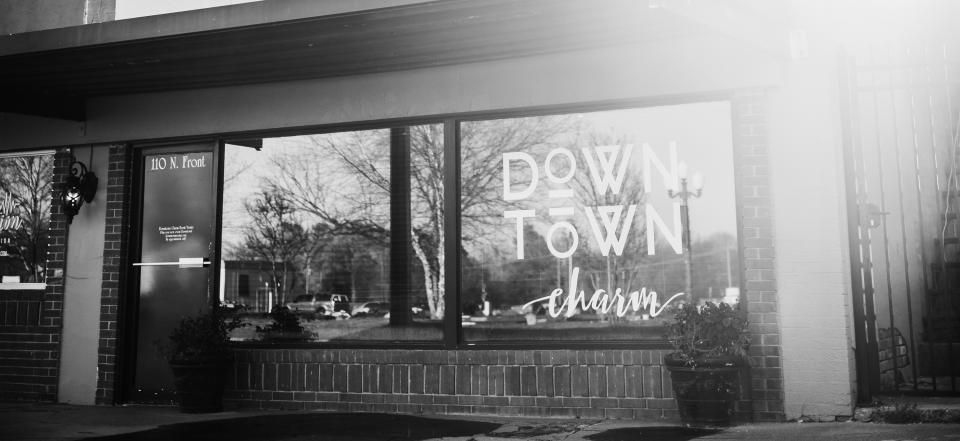 Black-and-white storefront window with a “Downtown” sign and bench outside.