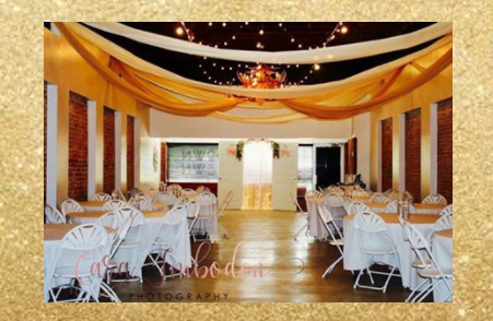 Elegant banquet hall with white chair covers, round tables, and gold draped ceiling decor