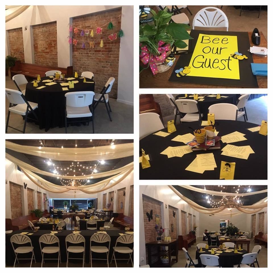 Decorated banquet hall with round tables, black chairs, yellow napkins, and a “Be Our Guest” sign