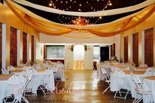 Decorated wedding reception venue with white tables, chairs, and gold drapes under string lights