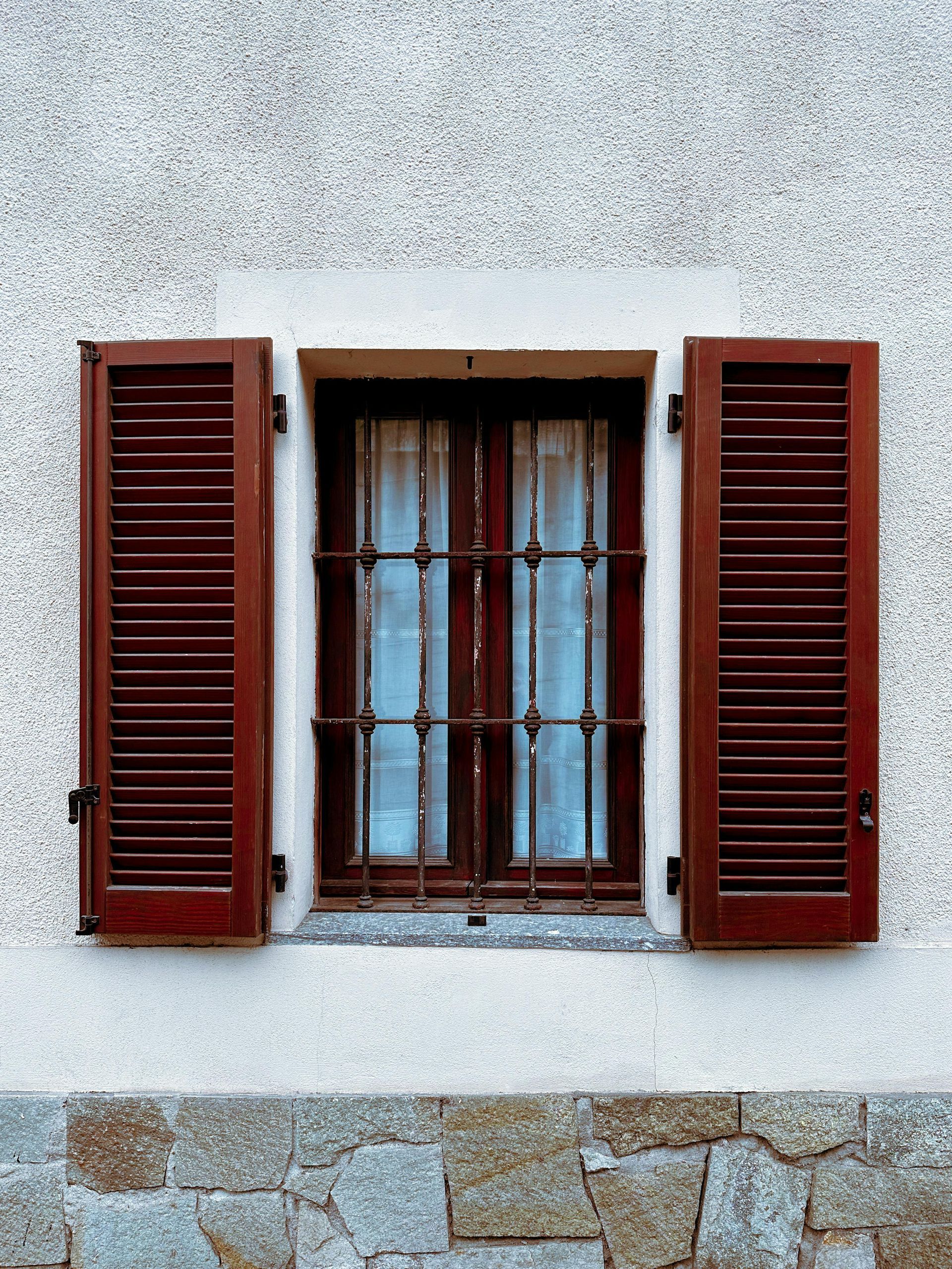 Two windows with green shutters on an orange building.