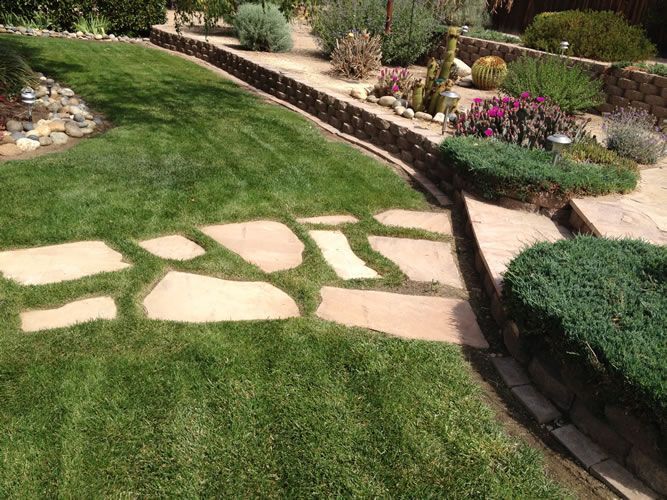 A lush green lawn with a stone walkway and a stone wall.