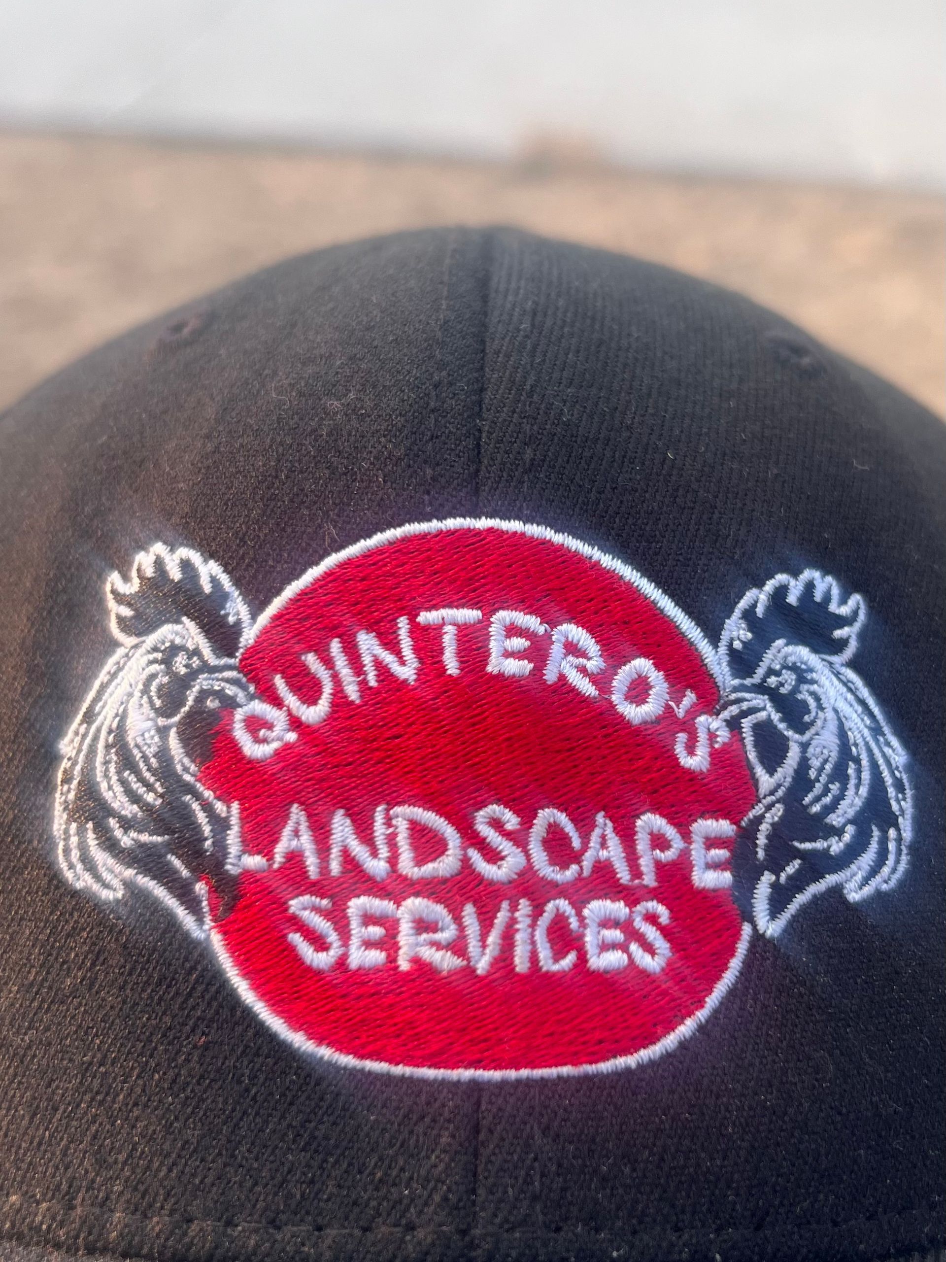 A black hat with a red circle that says quinteros landscape services