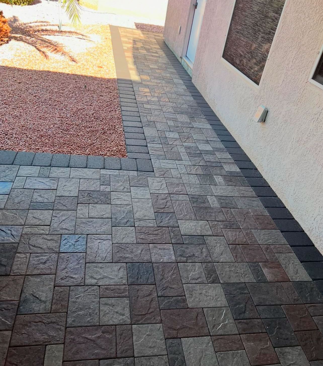 A brick walkway leading to a house with gravel in the background.
