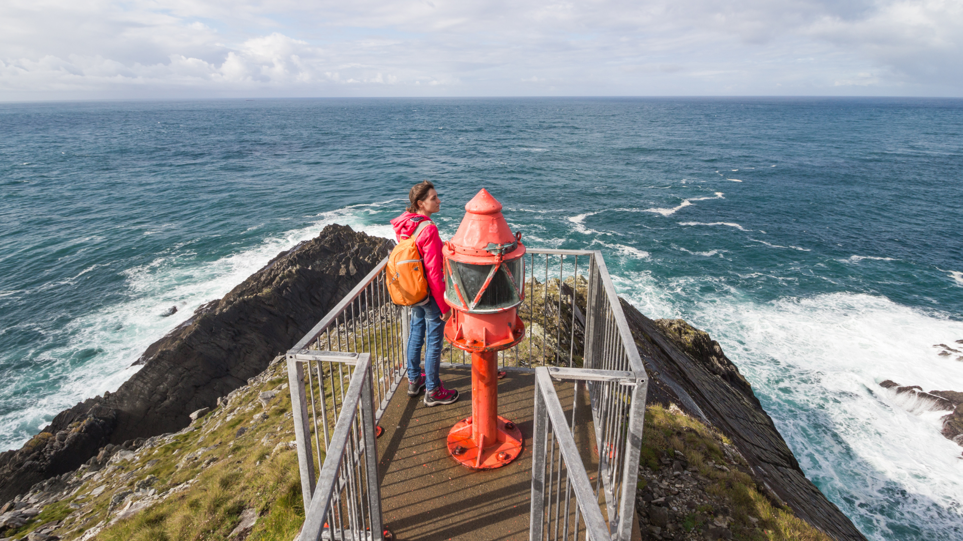 A woman is standing on top of a cliff overlooking the ocean.