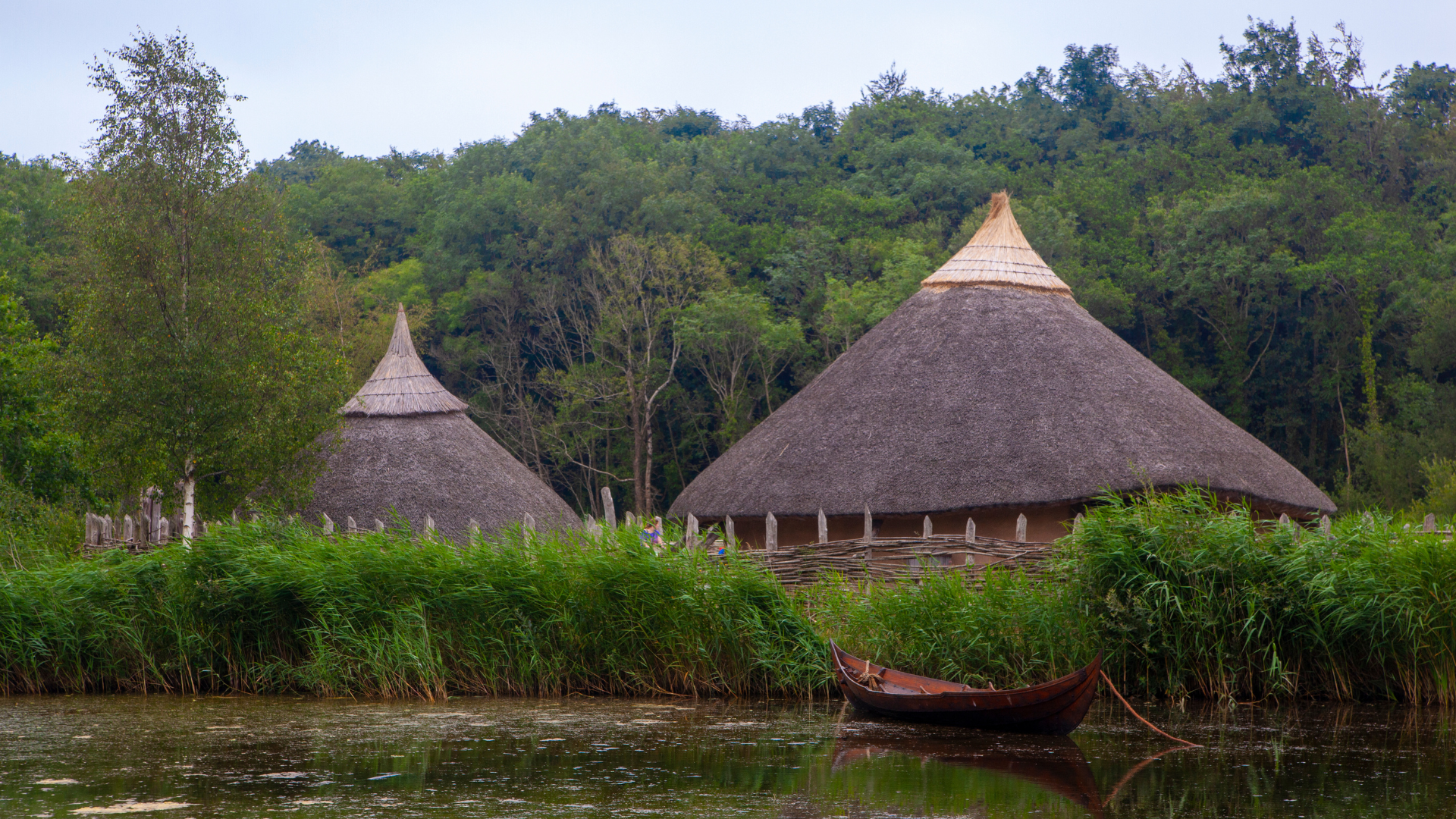 Two thatched huts are sitting on the shore of a lake.