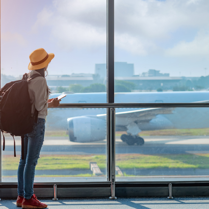 A woman is looking out of a window at an airplane on the runway.
