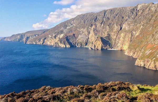 A cliff overlooking a body of water with mountains in the background.