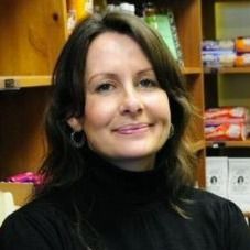 A woman in a black turtleneck is smiling in front of a bookshelf.