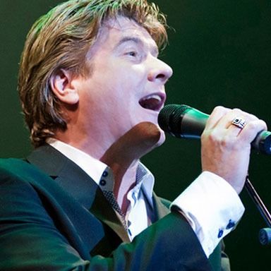 A man singing into a microphone with a ring on his finger