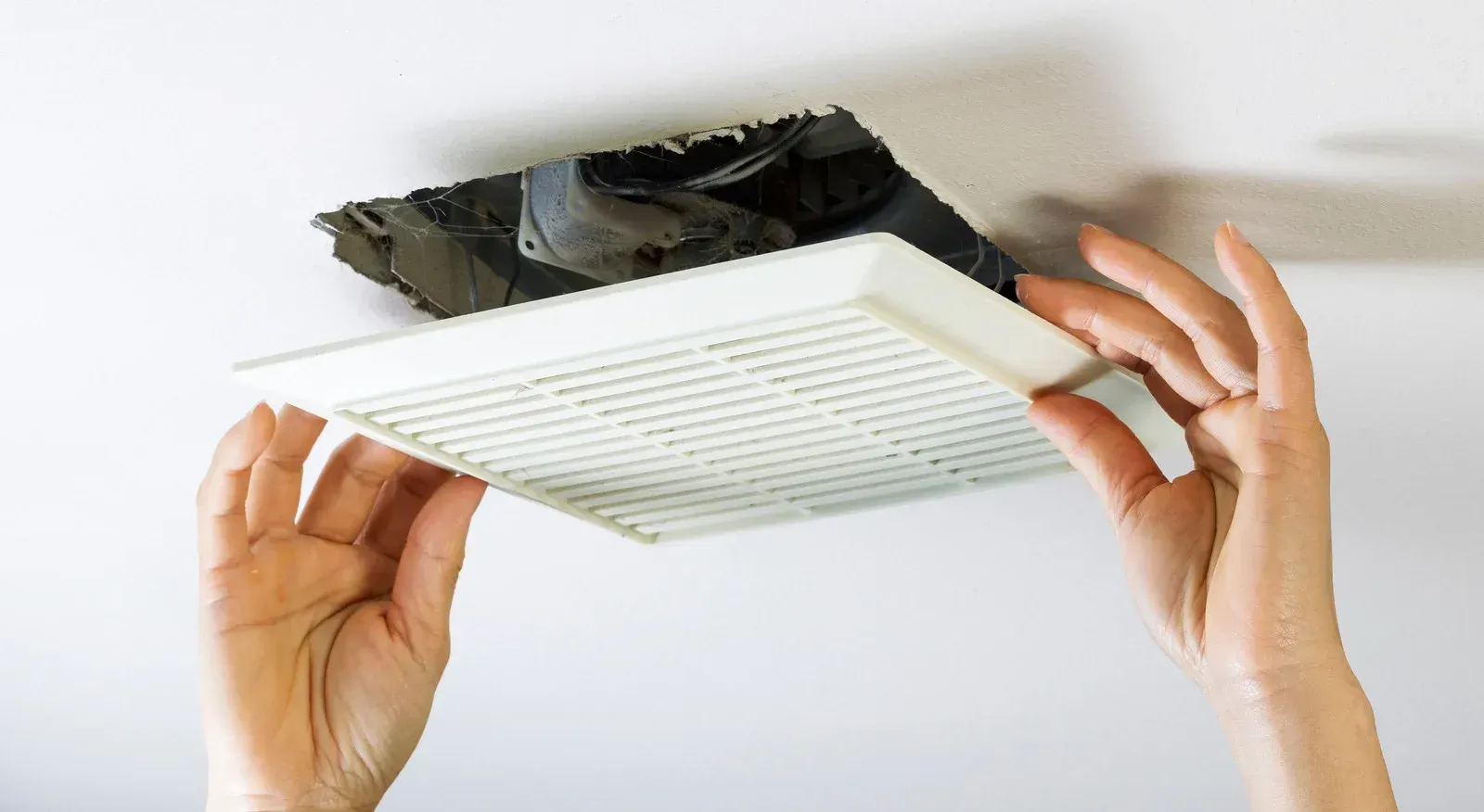 Hands installing a white ceiling air filter into a damaged vent opening