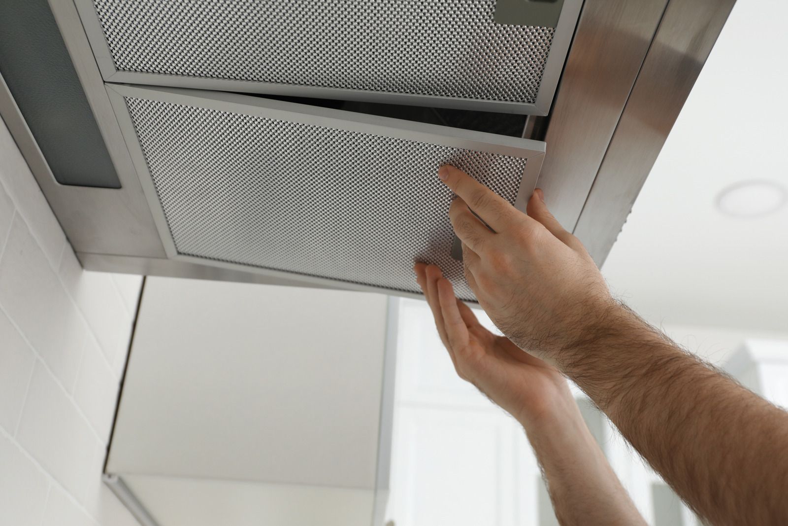 Hands removing a metal vent filter from a ceiling air vent
