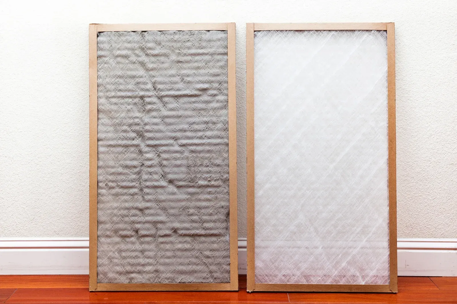 Two framed rectangular filters leaning against a wall on a wooden floor, one gray and one white