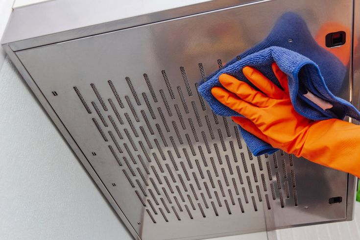 Orange-gloved hand wipes a metal ventilation panel with a blue cloth.