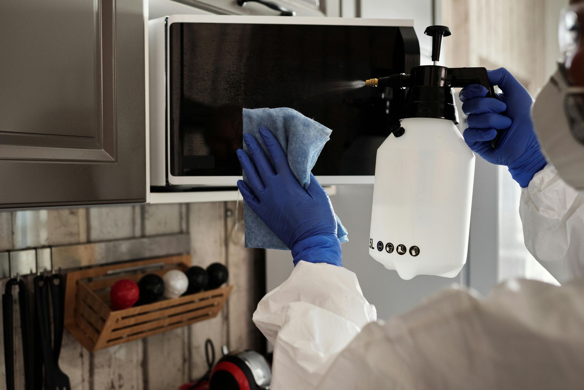 Person cleaning a microwave with a spray bottle and blue gloves in a kitchen